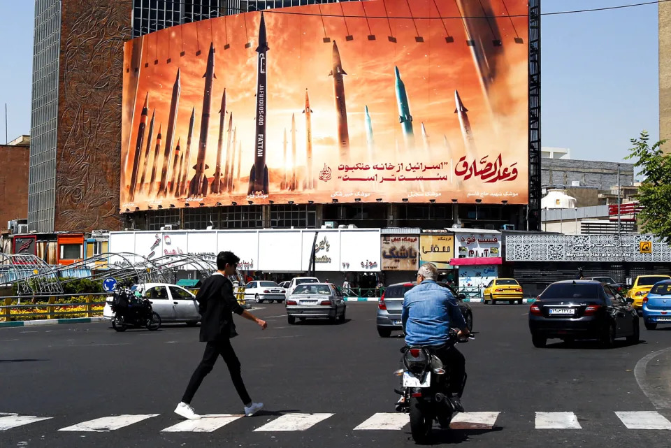 A man crosses a street as motorists drive past a billboard depicting Iranian ballistic missiles in service. (AFP via Getty Images)