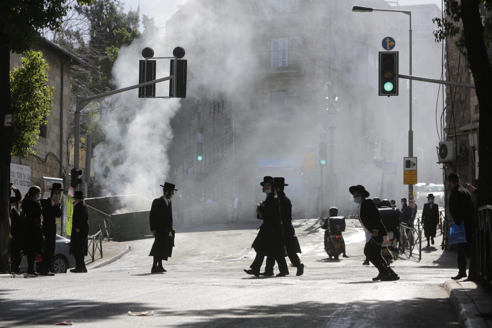 Men walk amid smoke from a dumpster fire, in an ultra-Orthodox neighborhood in Jerusalem, Sunday, Jan. 24, 2021. Ultra-Orthodox demonstrators clashed with Israeli police officers dispatched to close schools in Jerusalem and Ashdod that had opened in violation of health regulations on Sunday. (AP Photo/Sebastian Scheiner)