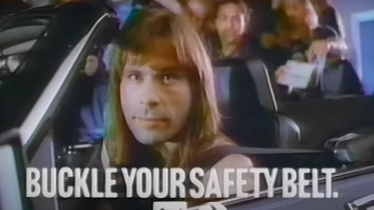  Iron Maiden singer Bruce Dickinson sat in a convertible and looking at the camera, with text reading "Buckle your safety belt.". 