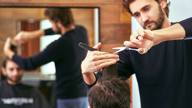 A barber cuts a man's hair with scissors.