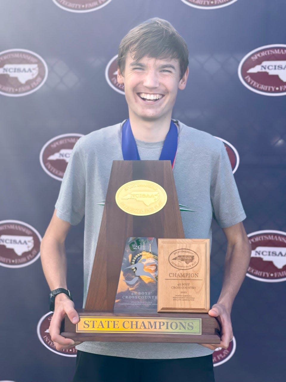 Christ School junior Rocky Hansen, the 2021 All-WNC cross country Runner of the Year, poses with trophies after winning the NCISAA Div. 4 state championship.
