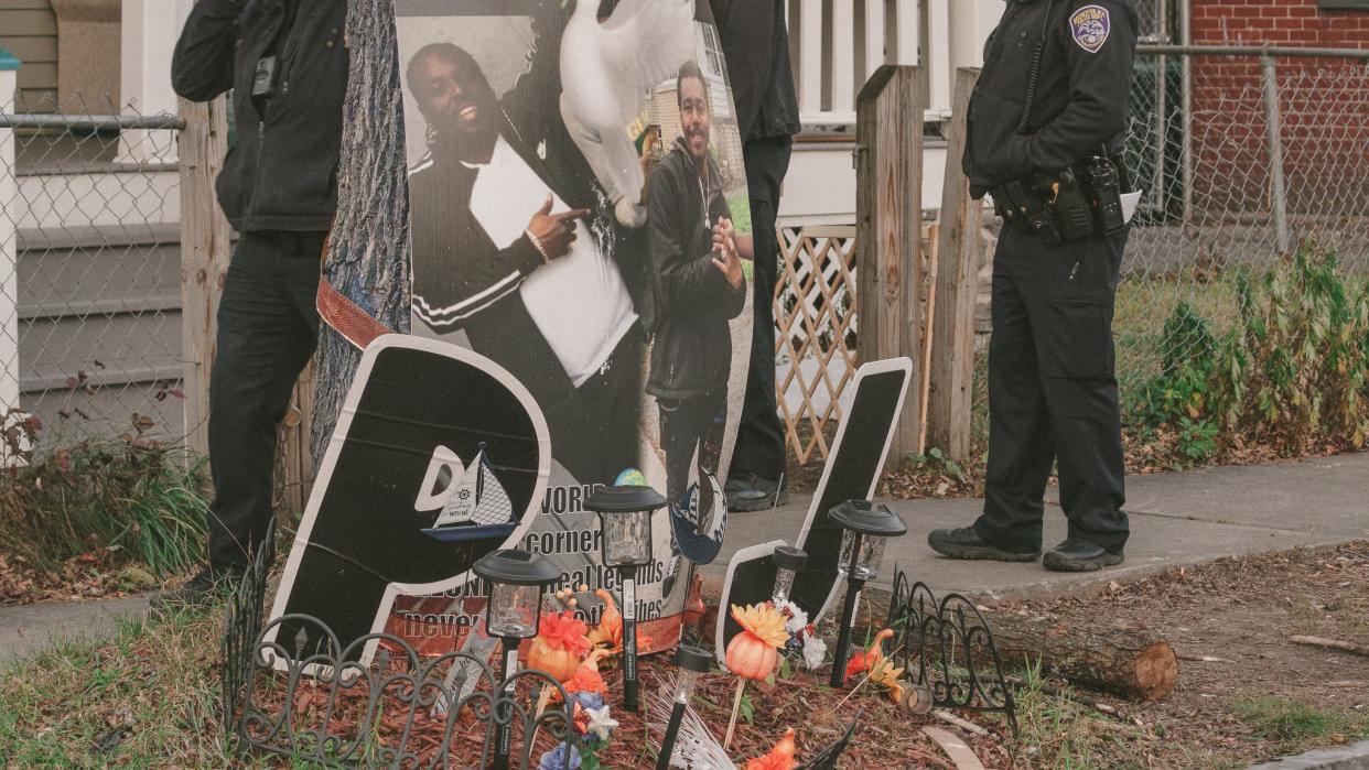 Rochester Police officers stand outside on Weld Street behind a memorial for a young man murdered due to gun violence.