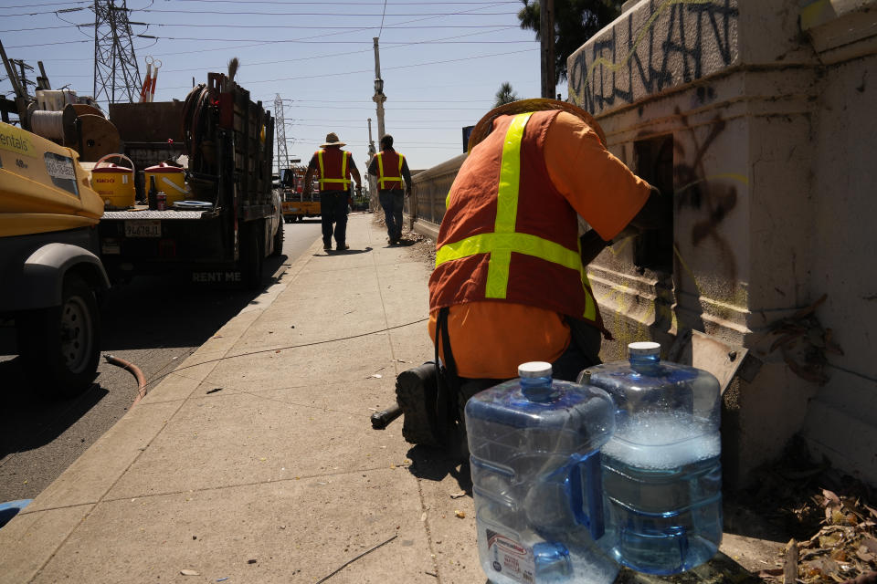 Electricians with IBEW Local 11 pull out an old copper cable line under excessive heat from the old Cesar Chavez Avenue Viaduct in Los Angeles, Thursday, July 13, 2023. Employers were reminded to adhere to regulations that require outdoor workers are given water, shade and regular breaks to cool off. The state will be performing spot checks at work sites to make sure the rules are being followed, said Jeff Killip with the Division of Occupational Safety & Health. Water bottles on the ground contain soapy water used to facilitate the pulling of electric wires. (AP Photo/Damian Dovarganes)
