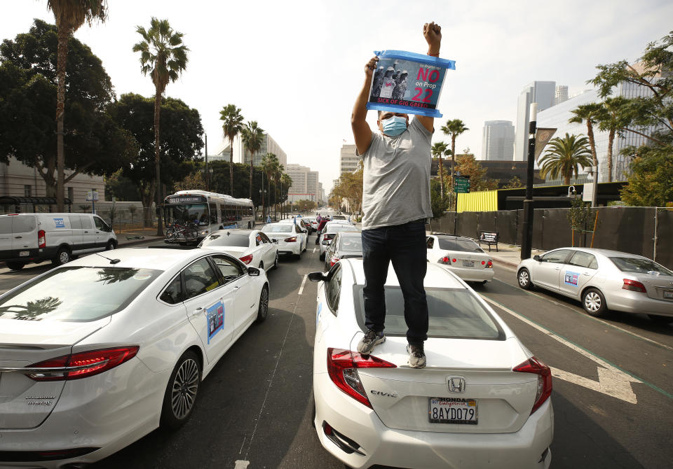 LOS ANGELES, CA - OCTOBER 08:    Rideshare driver Jesus Ibarra stands on his car in support as app based gig workers held a driving demonstration with 60-70 vehicles blocking Spring Street in front of Los Angeles City Hall urging voters to vote no on Proposition 22, a November ballot measure that would classify app-based drivers as independent contractors and not employees or agents, providing them with an exemption from Californias AB 5. The action is part of a call for stronger workers rights organized by the Mobile Workers Alliance with 19,000 drivers in Southern California and over 40,000 in all of California.      Los Angeles on Thursday, Oct. 8, 2020 in Los Angeles, CA. (Al Seib / Los Angeles Times