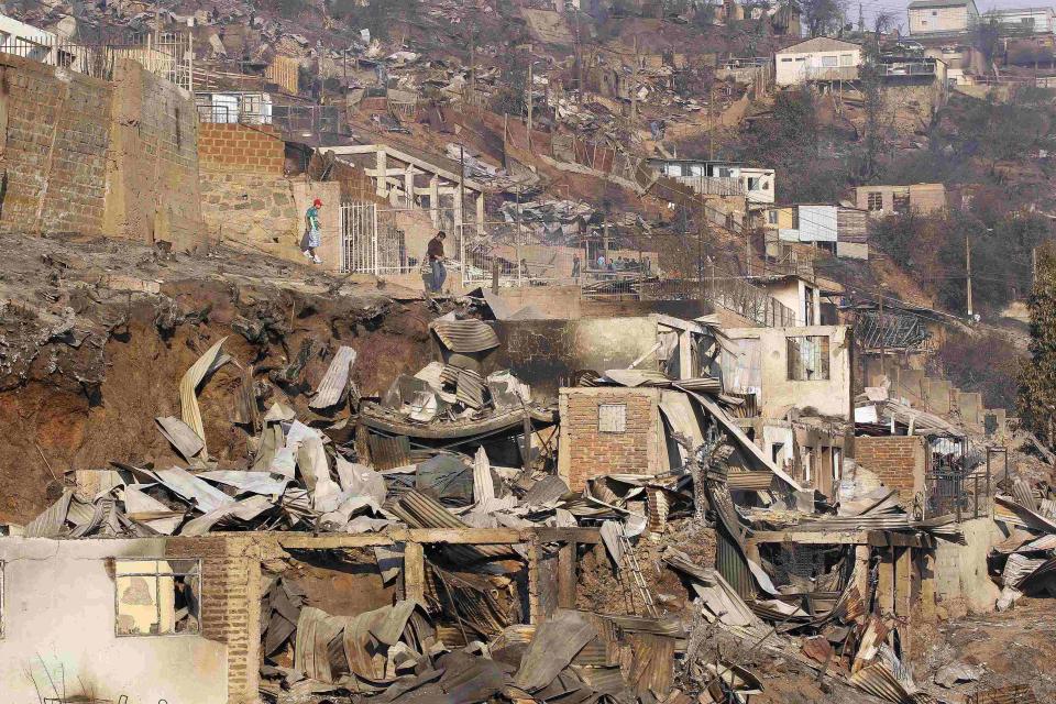 People walk amidst burnt houses after a forest fire in Valparaiso city, northwest of Santiago, April 13, 2014. At least 11 people were killed and 500 houses destroyed over the weekend by the fire that ripped through parts of Chilean port city Valparaiso, as authorities evacuated thousands and used aircraft to battle the blaze REUTERS/Eliseo Fernandez (CHILE - Tags: ENVIRONMENT DISASTER)