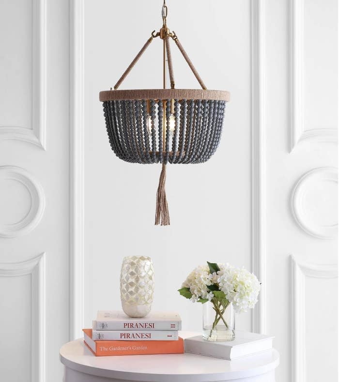 A boho-style chandelier hangs above a stack of books on a table with a vase of flowers