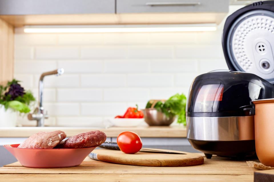 Multicooker and air fryer on wooden table in a modern kitchen. Kitchenware with vegetables and meat for cooking. Naturals products: pepper, greens, tomatoes.