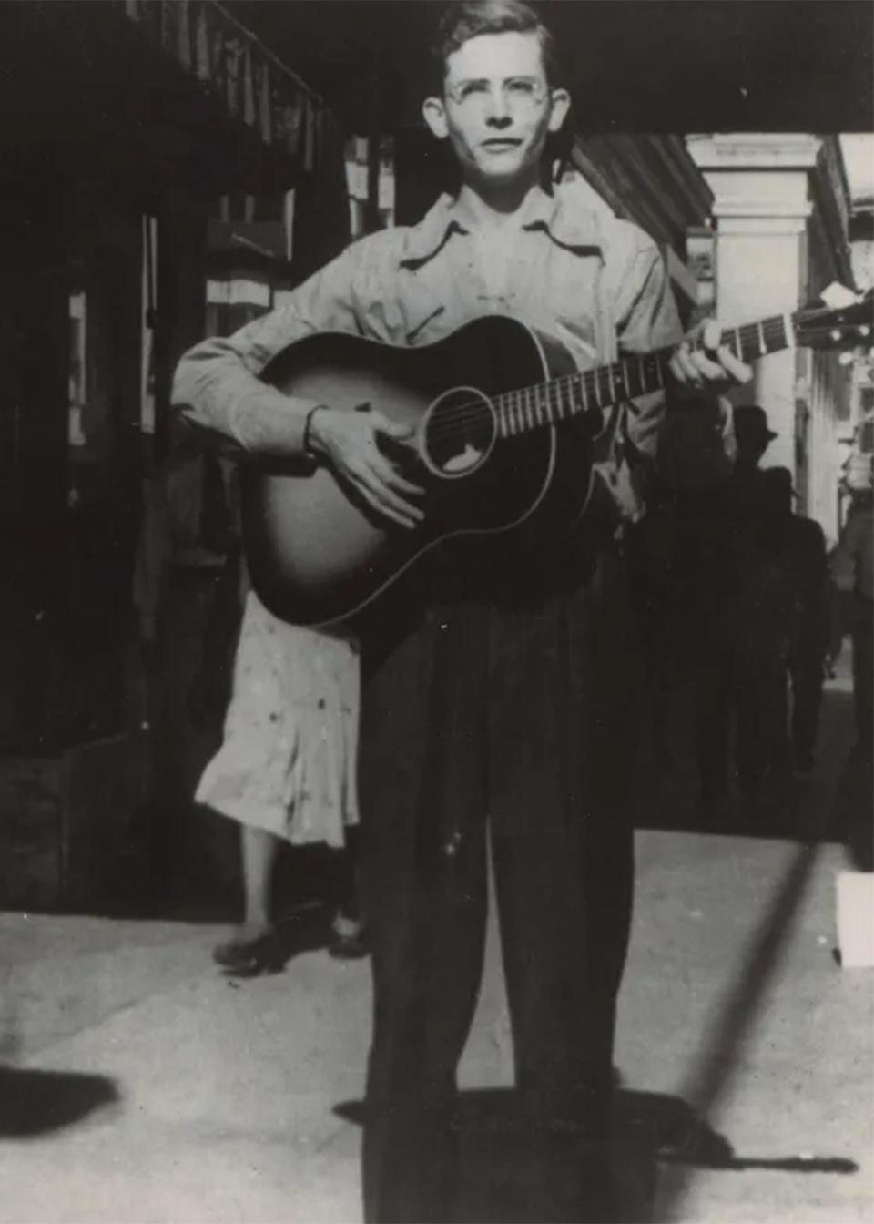 Hank Williams with a guitar on a sidewalk in Montgomery.