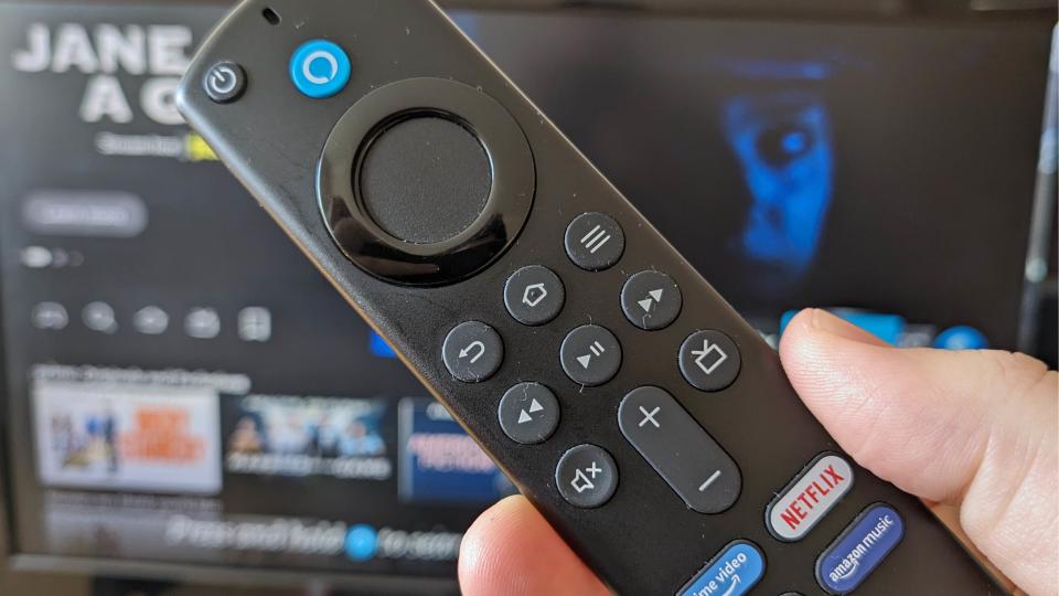  The Fire TV Stick 4K remote held in front of a TV displaying Fire TV. 