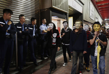 Pro-democracy protesters wearing Guy Fawkes masks walk past policemen on a road occupied by protesters as part of the Occupy Central civil disobedience movement at Mongkok shopping district November 5, 2014, the day marking Guy Fawkes Night. REUTERS/Bobby Yip