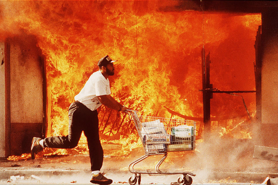 Man pushing cart past burning market