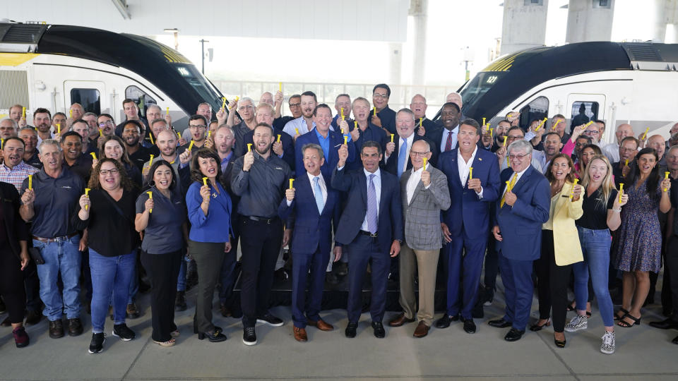 Mayors of cities along the Brighline route, Brightline and Orlando Airport Executives, VIP's and Brightline employees hold up souvenir golden railroad spikes as they pose for a photo to celebrate the completion of the construction of the Brightline high speed rail on Wednesday, June 21, 2023, in Orlando, Fla. The rail system now connects Miami to Orlando. (AP Photo/John Raoux)