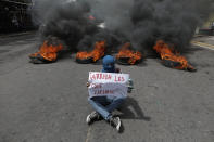 FILE - In this Oct. 24 2019, file photo, man holds a sign that reads in Spanish "Hurray for those who fight" as he sits in front of a street blocked by a burning barricade, during a protest to demand the resignation of President Juan Orlando Hernandez, in Tegucigalpa, Honduras. From Honduras to Chile, popular frustration with anemic economic growth, entrenched corruption and gaping inequality is driving the region’s middle classes to rebel against incumbents of all ideological bents in what has been dubbed by some the Latin American Spring. (AP Photo/Elmer Martinez, File)