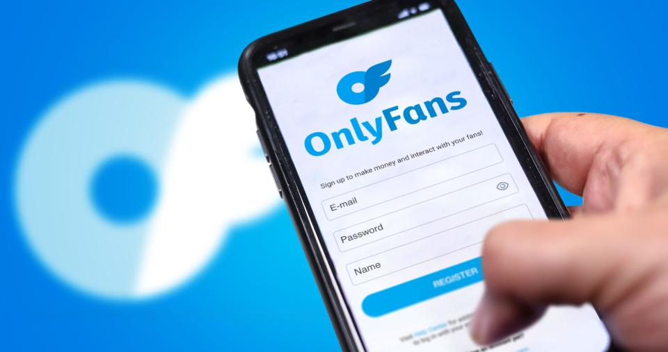London, UK, August 2021; a hand holds a mobile phone with the OnlyFans registration form on the screen and the logo blurred in the background. OnlyFan