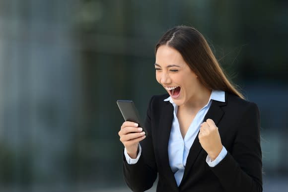 Well-dressed businesswoman fist-pumps in excitement over news she is reading on her smartphone.