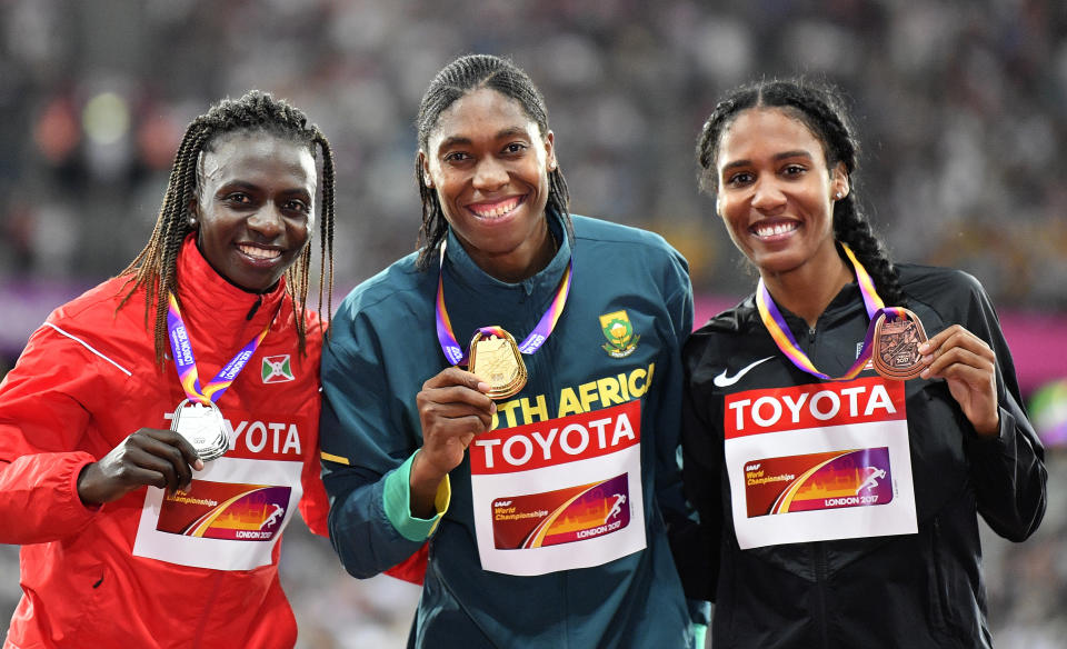 FILE - In a Sunday, Aug. 13, 2017 file photo, Women's 800 meters gold medalist South Africa's Caster Semenya, center, stands with silver medalist Burundi's Francine Niyonsaba, left, and bronze medalist United States' Ajee Wilson, right, on the podium at the World Athletics Championships in London. Defending 800-meter champion Caster Semenya won't stand on the podium with a medal draped around her neck at the World Championships in Doha, Qatar. On the 10th anniversary of Semenya blowing away the field in the 800 at the 2009 World Championships in Berlin, she won't comply with the International Association of Athletics Federations' latest version of a regulation to lower her level of natural testosterone. (AP Photo/Martin Meissner, File)