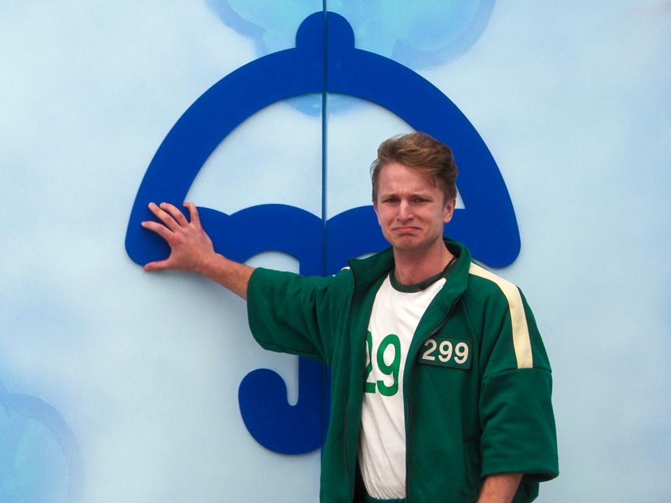 Man with sad face in a green tracksuit touching blue umbrella sign