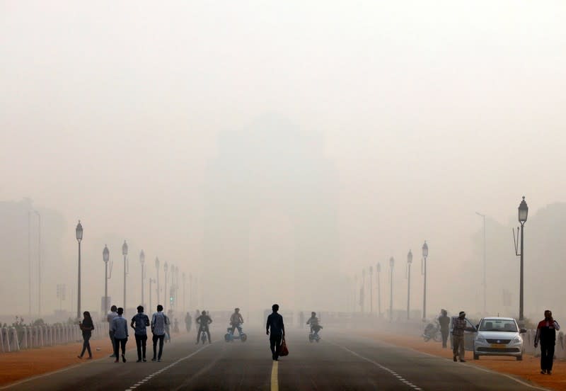 People walk in front of the smog covered India Gate war memorial in New Delhi