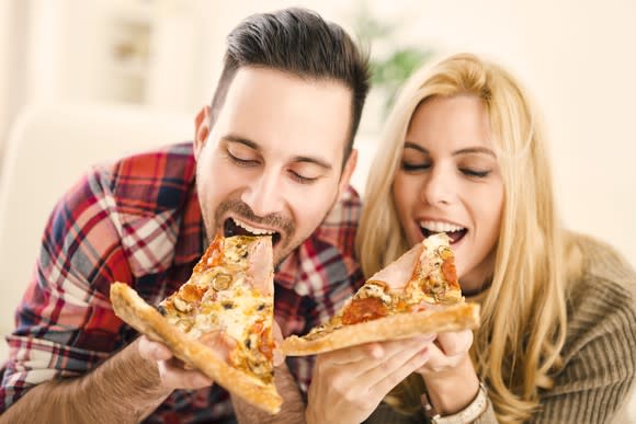 A man and woman each take a bite of pizza.