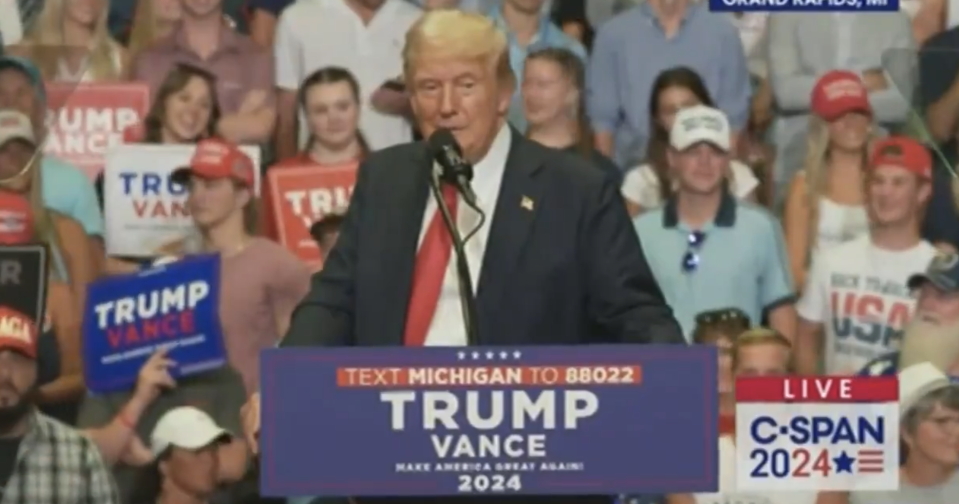 Donald Trump speaks at a rally in Grand Rapids, MI. Supporters hold various campaign signs