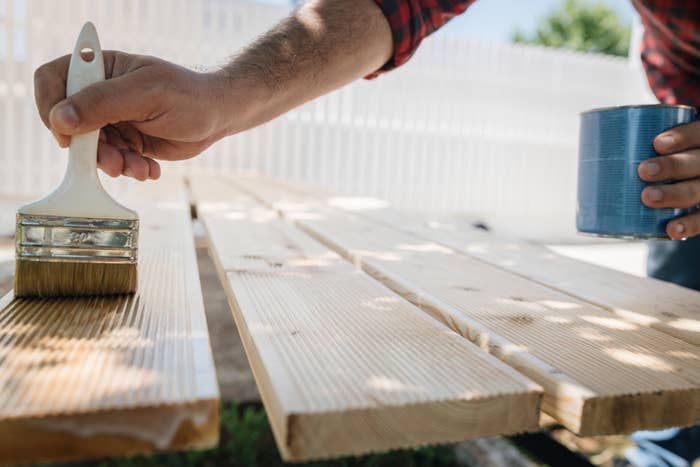 Person applying wood stain to boards with a brush