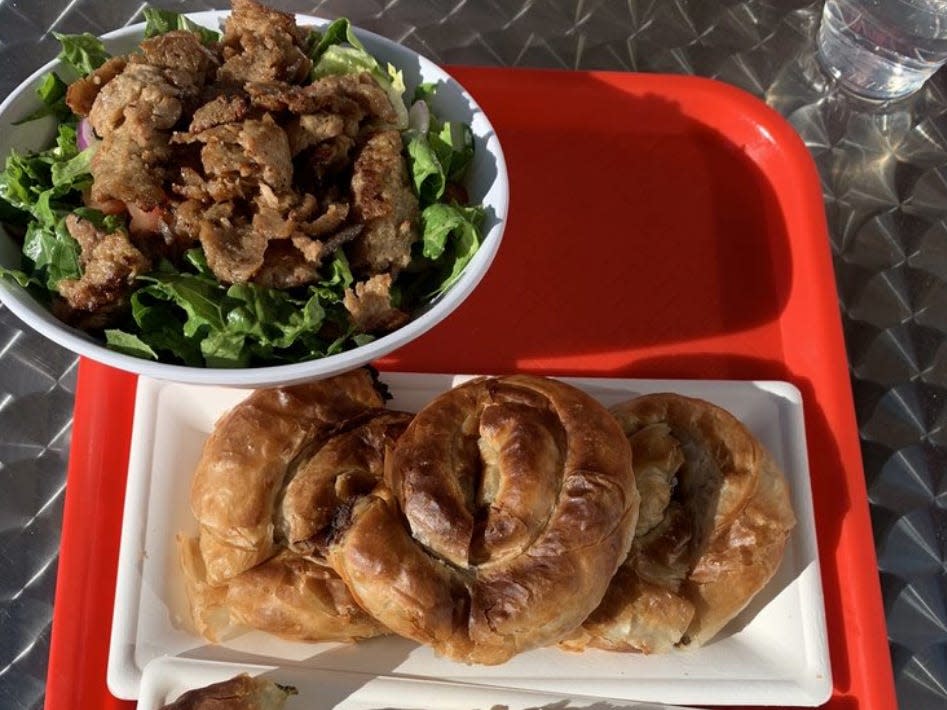 A bowl of salad and meat and a plate of spiral-shaped pastries on a red tray.