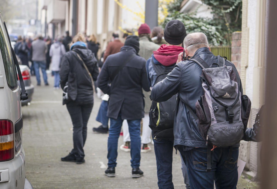 People wait in a long queue on the sidewalk at the Corona Test Center of the Medical On-call Service Hessen, Frankfurt, Germany, Tuesday, March 17, 2020. The test centers for corona virus smears in Hesse are overworked. Although the Association of Statutory Health Insurance Physicians (KV) is continuing to expand capacities, the bottleneck is the laboratories. Long queues form every morning. ( Frank Rumpenhorst/dpa via AP)
