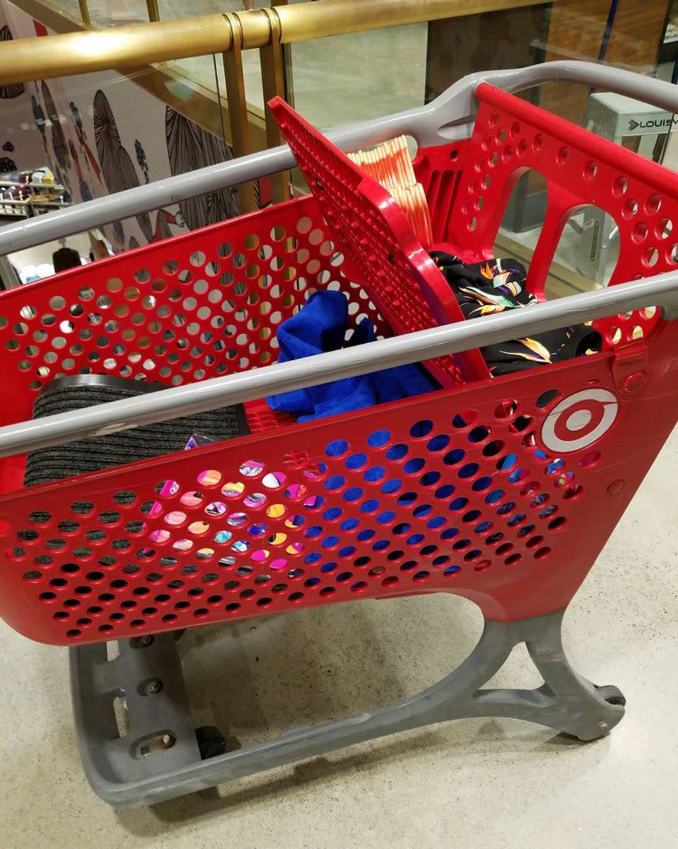 A red plastic cart with a few items in a Target store, beige floor and brass railing in the background