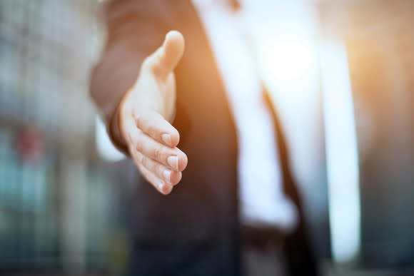 A person in a suit with an outstretched hand as if to shake hands with someone.