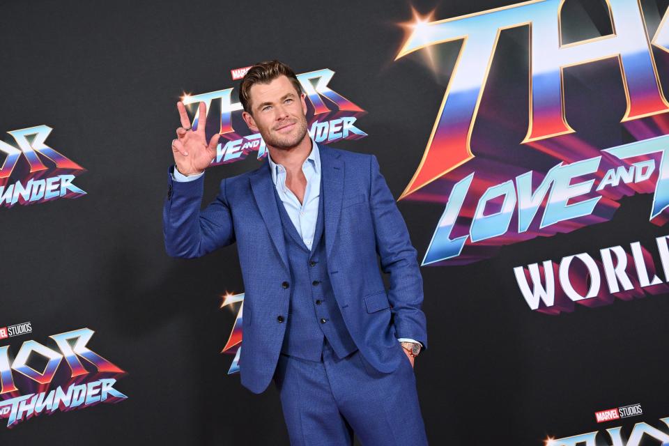 Chris Hemsworth in a blue suit and light blue shirt waving and smiling