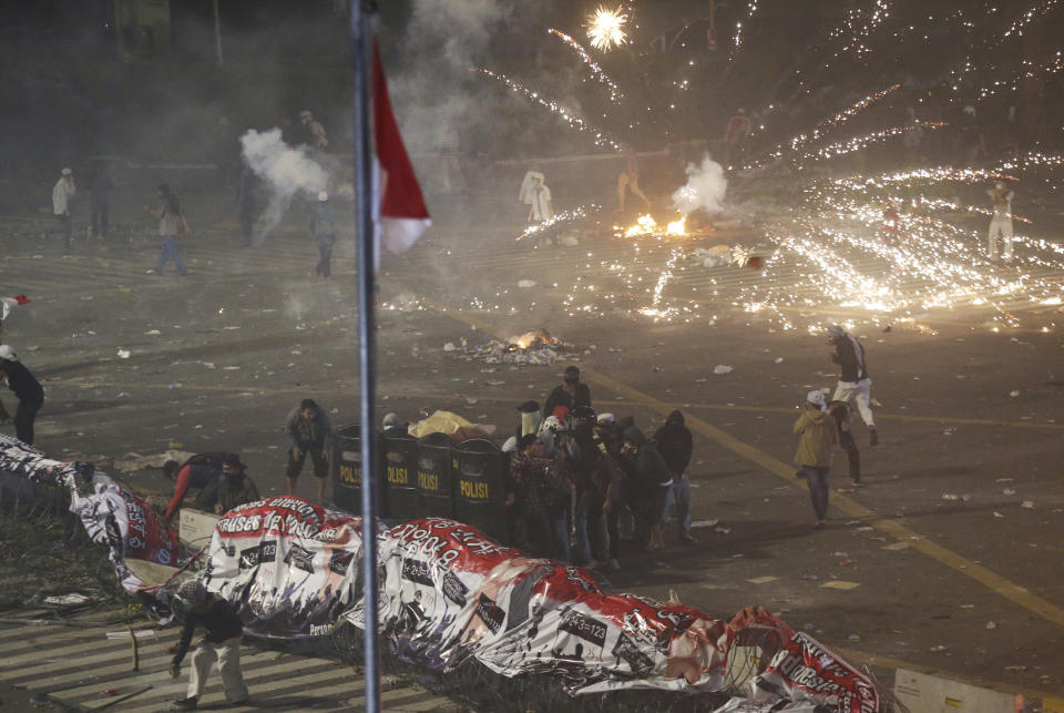 Supporters of the losing presidential candidate take cover with police shields as fireworks explode during clashes with police Wednesday, May 22, 2019, in Jakarta, Indonesia. Indonesian President Joko Widodo said authorities have the volatile situation in the country's capital under control after a number of people died Wednesday in riots by supporters of his losing rival in last month's presidential election. (AP Photo/Achmad Ibrahim)