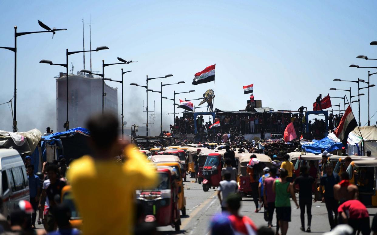 Protesters carry the Iraqi national flag as they gather on the Al-Jumhuriya bridge, which leads to the headquarters of the Iraqi government inside the high security Green Zone area - Shutterstock