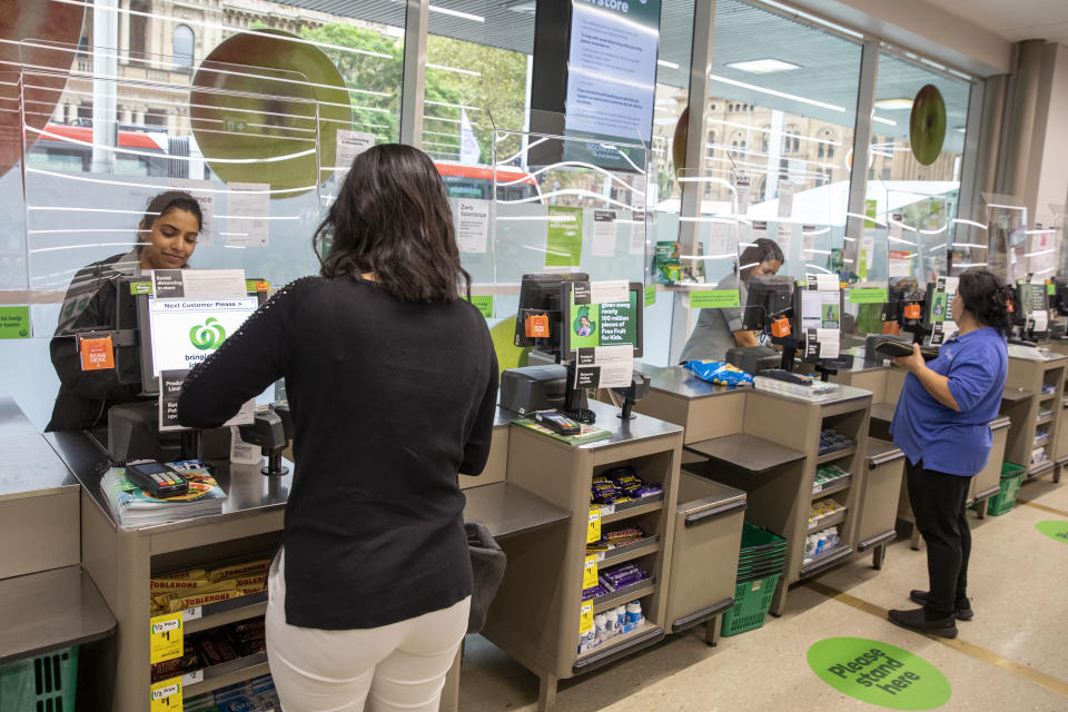 Photo shows Woolworths staff and customers interacting through a screen.