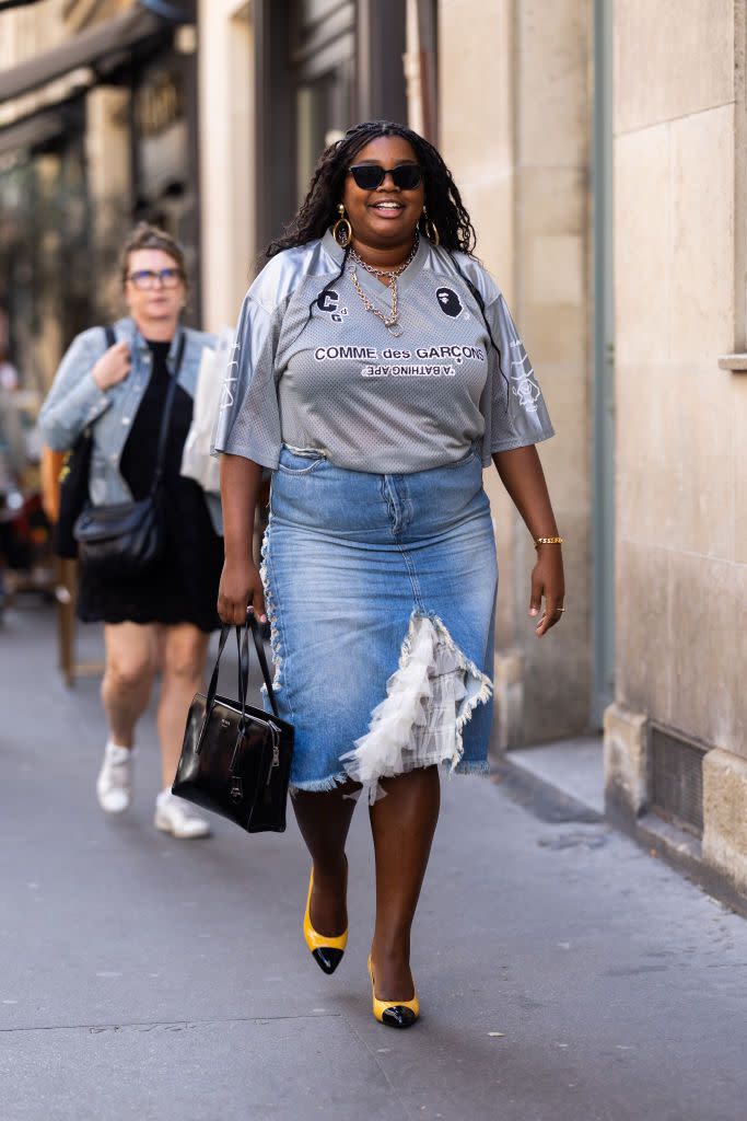 paris, france september 27 gabriella karefa johnson is seen wearing black sunglasses, a black leather prada bag, black and yellow shiny pumps, pendant gold earrings, a chain necklace, a gold bracelet, a gold ring, a grey football printed comme des garcons t shirt and a hight waist midi jeans skirt with white tulle applications on the front outside the row fashion show during the womenswear springsummer 2024 as part of paris fashion week on september 27, 2023 in paris, france photo by valentina frugiuelegetty images