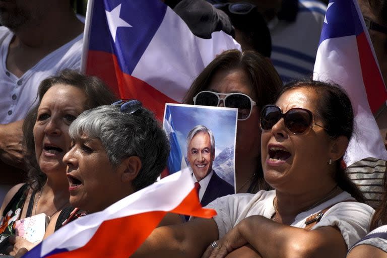 La gente canta el Himno Nacional frente al Congreso en Santiago, mientras aguarda para despedir al expresidente Sebastián Piñera 