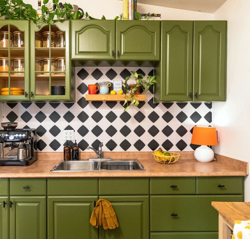 Green cabinets in kitchen with black and white backsplash.