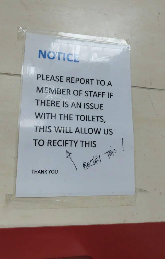 Notice on a wall asking to report toilet issues to staff. "Rectify this!" handwritten at the bottom