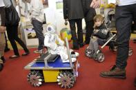 A child is fascinated by a mini robot designed as it parades around the fair on a miniature vehicle. It was developed by the School of Business and Engineering Vaud.