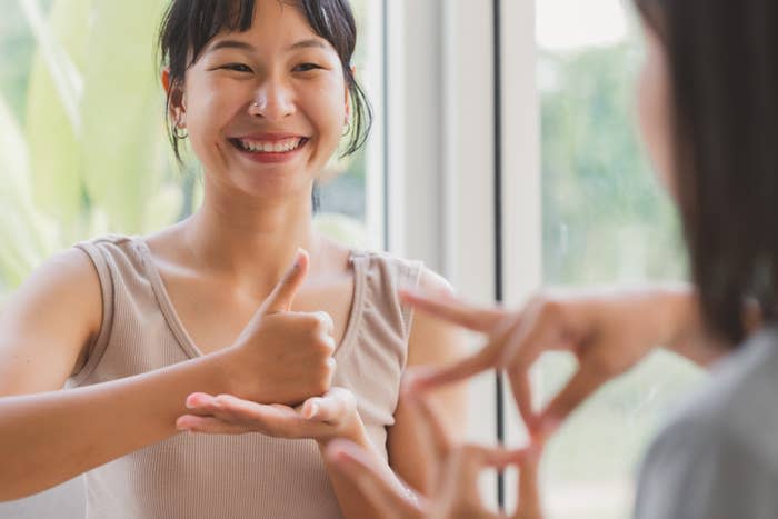 A woman smiling, signing in American Sign Language (ASL) with another person