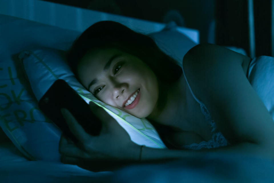 Smiling Woman Using Mobile Phone While Lying On Bed At Night