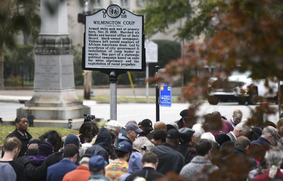 People stand under the new North Carolina highway historical marker to the 1898 Wilmington Coup during a dedication ceremony in Wilmington, N.C., Friday, Nov. 8, 2019. The marker stands outside the Wilmington Light Infantry building, the location where in 1898, white Democrats violently overthrew the fusion government of legitimately elected blacks and white Republicans in Wilmington. (Matt Born/The Star-News via AP)