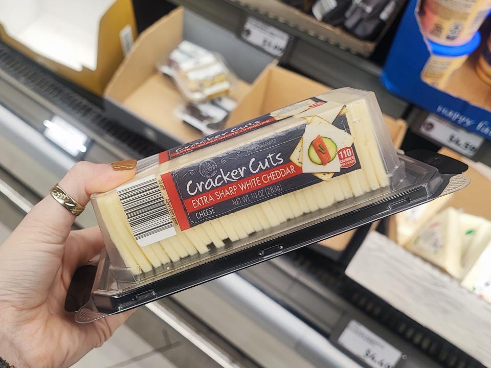 A hand holding a package of cracker cuts extra-sharp white-cheddar cheese.