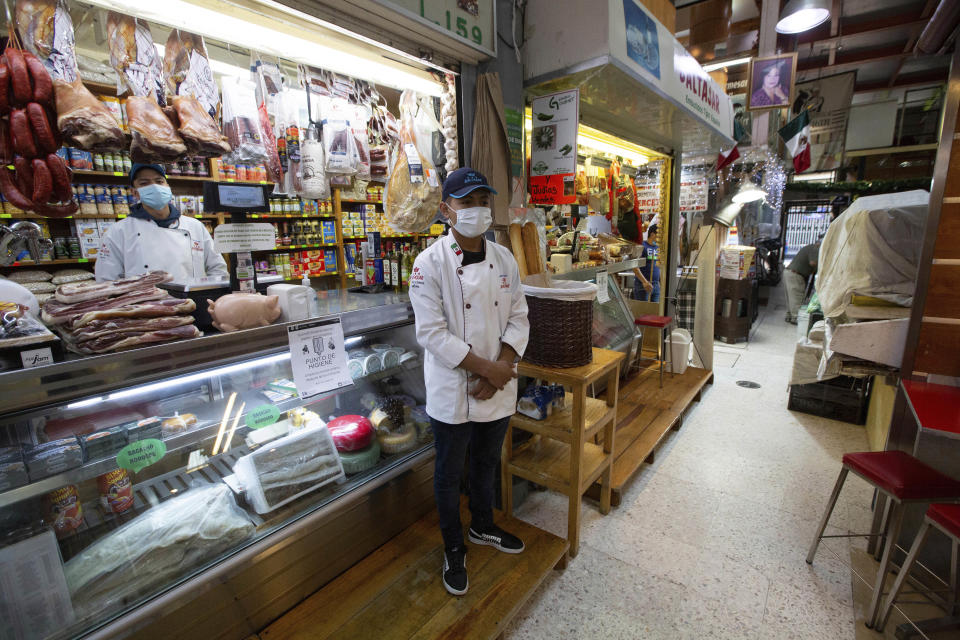 Vendors wearing protective face masks wait for shoppers at the popular San Juan food market in Mexico City, Wednesday, March 25, 2020. Mexico's capital has shut down museums, bars, gyms, churches, theaters, and other non-essential businesses that gather large numbers of people, in an attempt to slow the spread of the new coronavirus. (AP Photo/Fernando Llano)