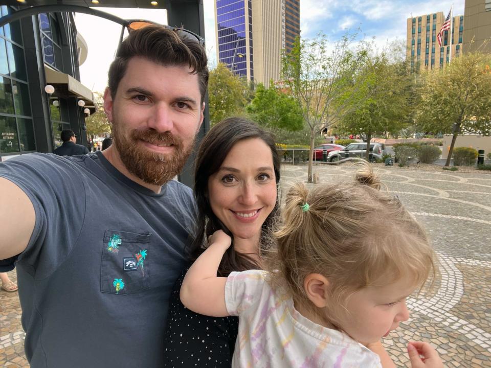 A family of three takes a selfie in a city.