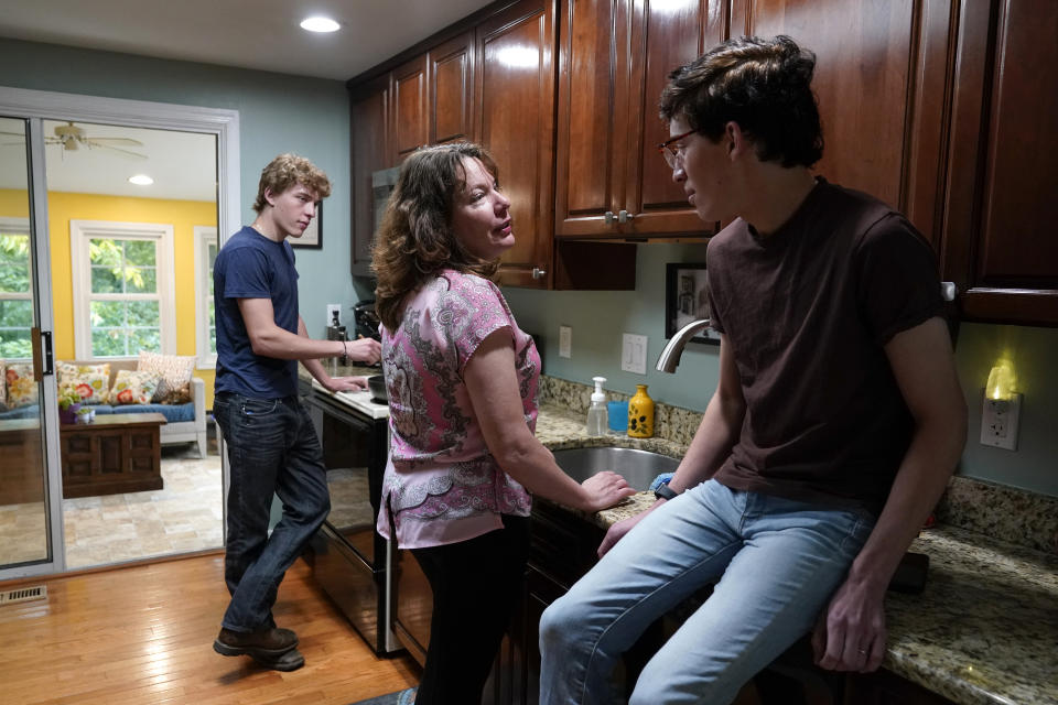 Julie Akey, center, visits with her sons, Sam and Theo, in their home in Herndon, Va., Tuesday, June 22, 2021. Akey is committed to searching for definitive links between her illness and her military service. But the cancer and harsh treatments are taxing on her body and mind, the research emotionally draining. (AP Photo/Patrick Semansky)