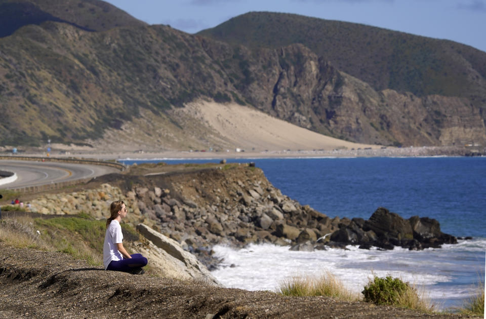 A woman sits alone in front of the ocean along Pacific Coast Highway, Monday, March 23, 2020, in Malibu, Calif. Officials are trying to dissuade people from using the beaches after California Gov. Gavin Newsom ordered the state's residents to stay at home indefinitely. His order restricts non-essential movements to control the spread of the coronavirus that threatens to overwhelm the state's medical system. (AP Photo/Mark J. Terrill)
