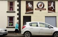 A woman walks past empty buildings which have been covered with artwork to make them look more appealing, in the village of Bushmills on the Causeway Coast August 19, 2013. One of the homes of Irish whiskey has taken a scheme developed in Northern Ireland of erecting fake shop fronts where derelict buildings lie and has truly run with it in a bid to woo tourists. Bushmills, best known as the village where the whiskey of the same name was distilled for the first time 400 years ago, is now also becoming recognisable for the artwork and graphics that brighten up shop fronts left empty during the economic downturn. Picture taken August 19, 2013. REUTERS/Cathal McNaughton (NORTHERN IRELAND - Tags: BUSINESS SOCIETY TRAVEL) ATTENTION EDITORS: PICTURE 17 OF 20 FOR PACKAGE 'NORTHERN IRELAND'S TROMPE L'OEIL' SEARCH 'BUSHMILLS ART' FOR ALL IMAGES