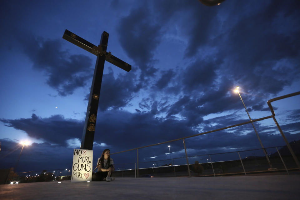 A woman sits next to a sign with a message that reads: ¨No More Guns! Make Love¨, in Juarez, Mexico, Saturday, Aug. 3, 2019, where people are gathering for a vigil for the 3 Mexican nationals who were killed in an El Paso shopping-complex shooting. Twenty people were killed and more than two dozen injured in a shooting Saturday in a busy shopping area in the Texas border town of El Paso, the state’s governor said. (AP Photo/Christian Chavez)