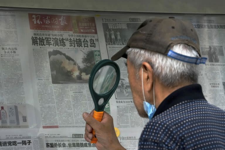 Un hombre usa una lupa para leer un periódico que informa sobre ejercicios militares de China alrededor de Taiwán, en Beijing, el 7 de agosto de 2022. (Foto AP/Andy Wong)