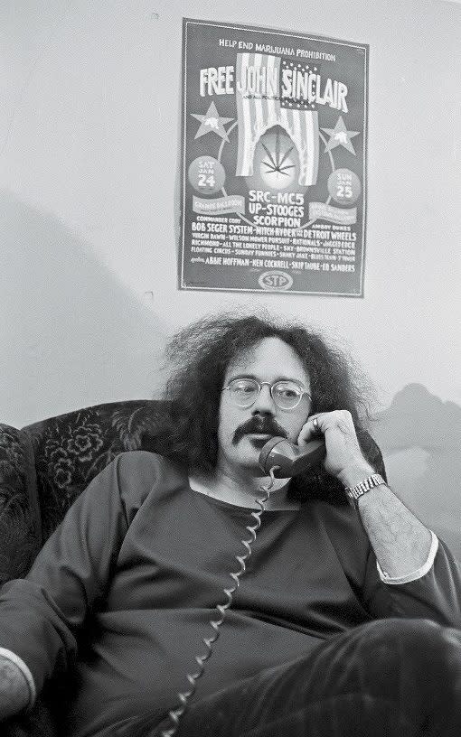 Sinclair in the 1970s beneath a poster advertising the Ann Arbor benefit gig